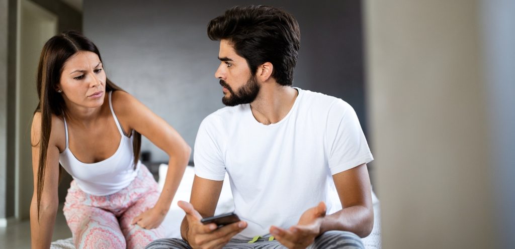 رجل يمسك هاتفه وزوجته تنظر إليه