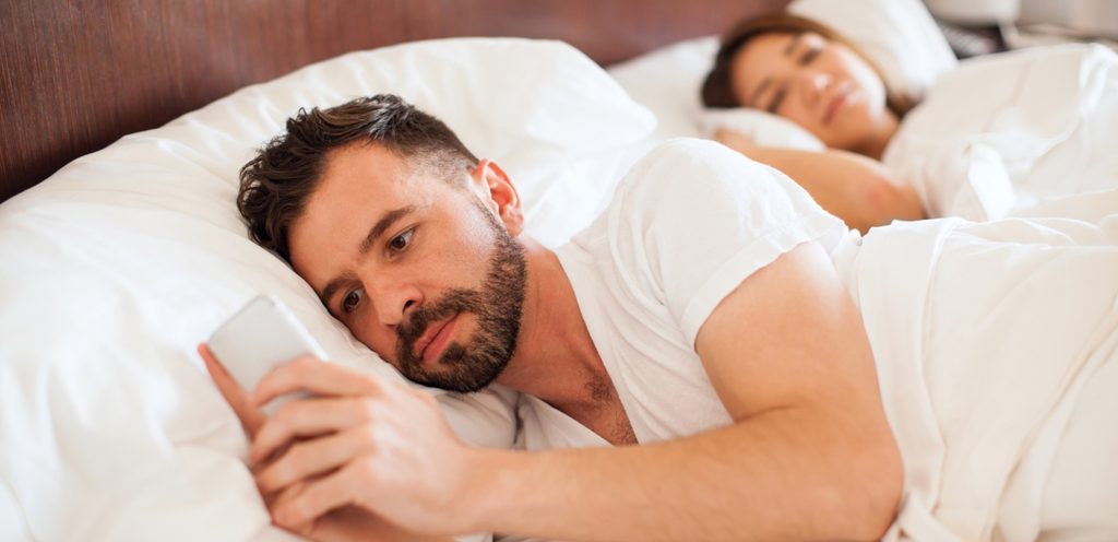 امرأة نائمة وزوجها مستلقٍ بجانبها يمسك الجوال