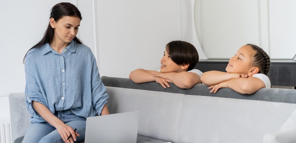 امرأة تعمل على الحاسوب وطفليها بجانبها