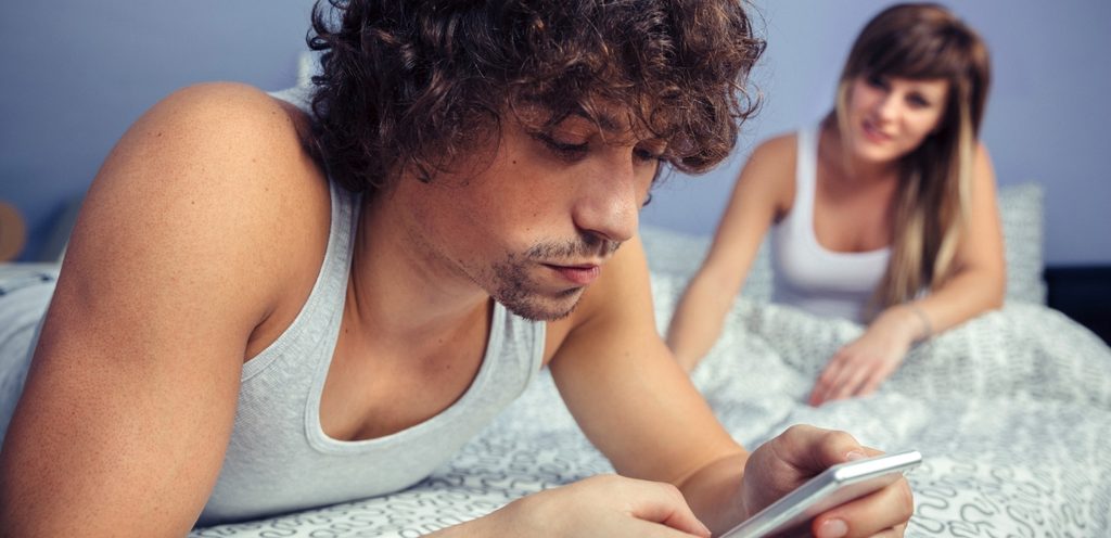 رجل يمسك هاتفه وزوجته تجلس خلفه