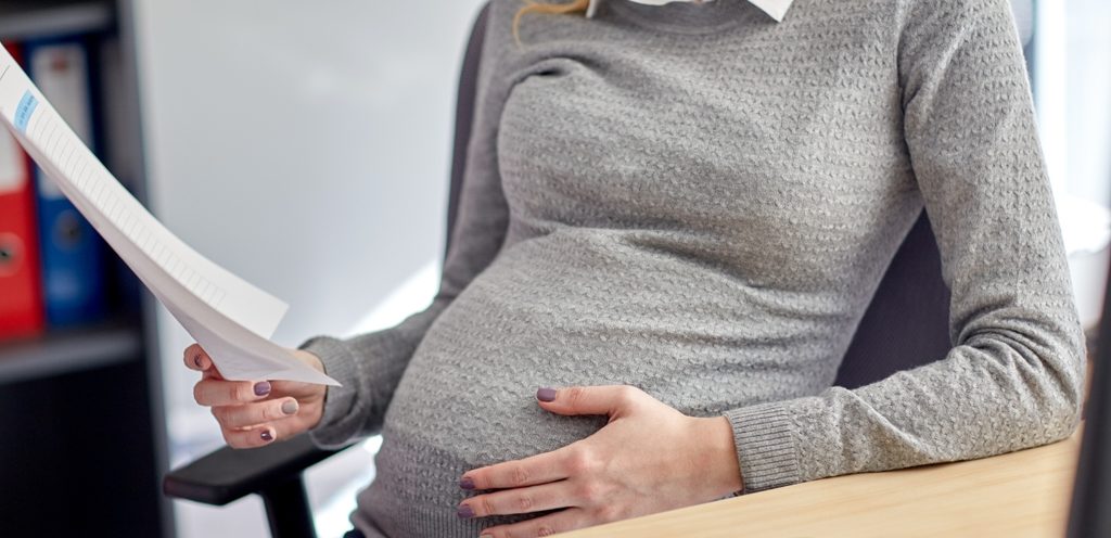 امرأة حامل تجلس خلف مكتب وتمسك أوراقًا