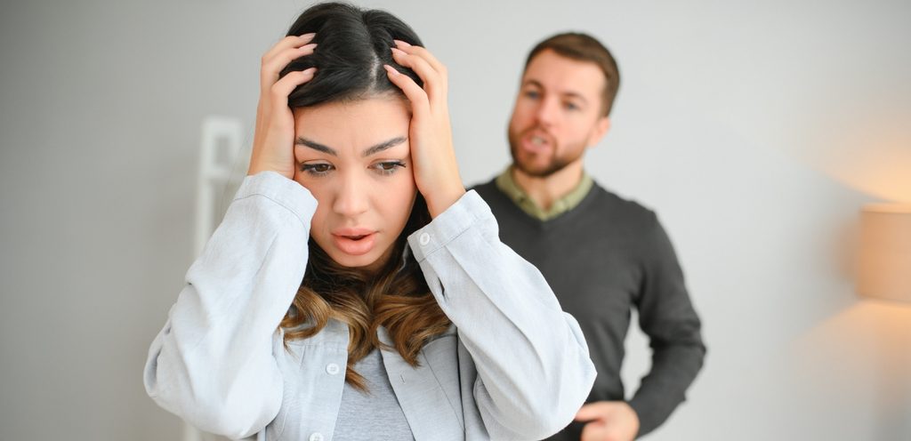 امرأة حزينة وزوجها خلفها يتكلّم بغضب