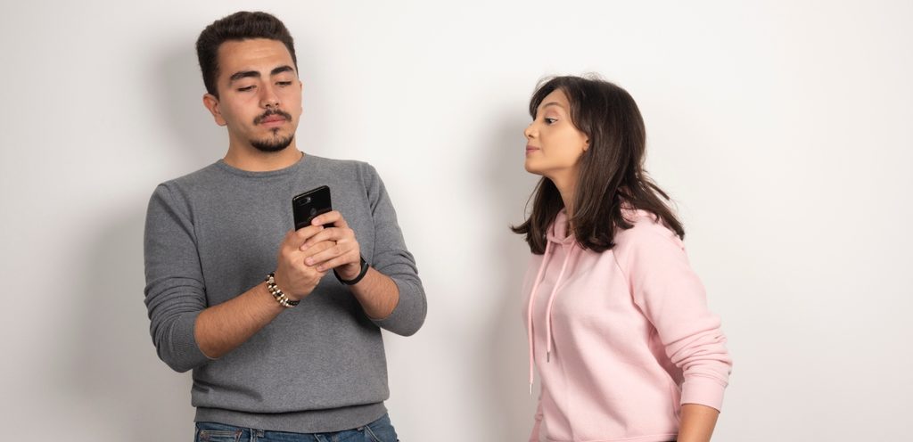 امرأة تنظر إلى زوجها الذي يستخدم هاتفه