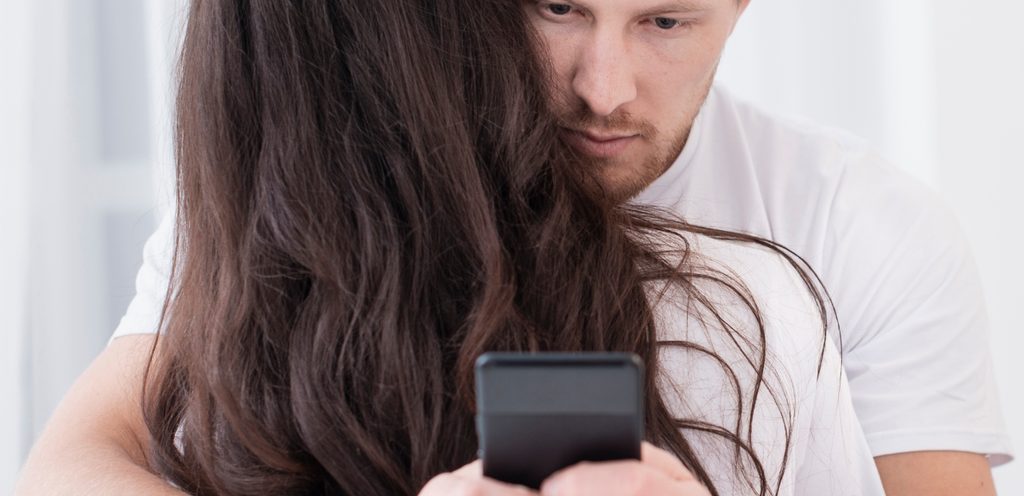 رجل يعانق زوجته ويستخدم جوّاله