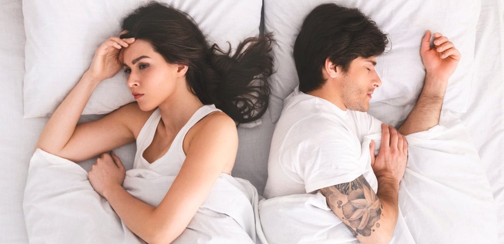 امرأة حزينة مستلقية بجانب زوجها النائم في السرير