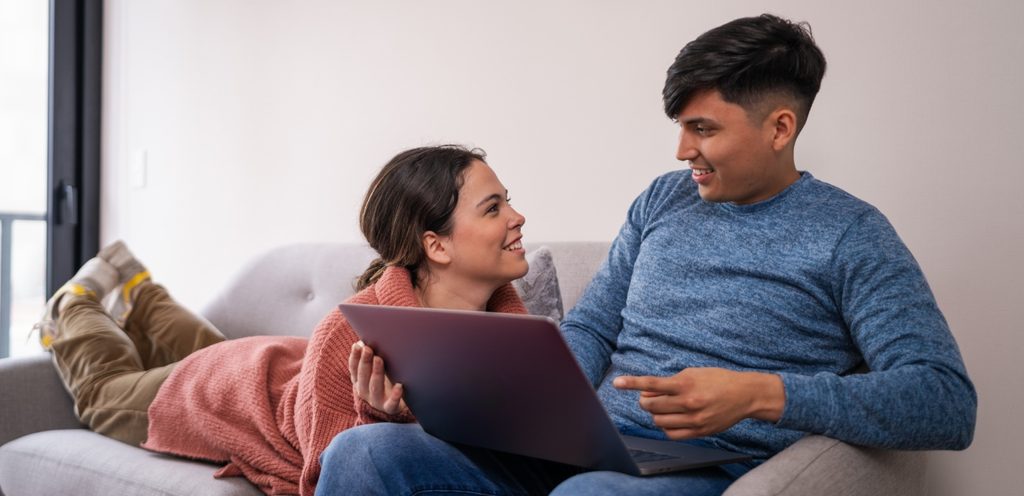 رجل يعمل على الحاسوب وزوجته سعيدة تنظر إليه وتجلس بجانبه