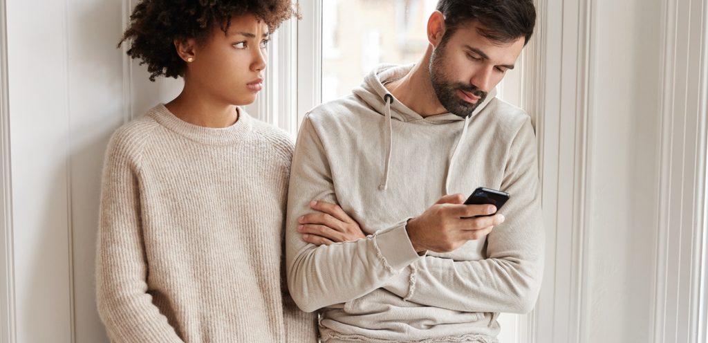 امرأة تنظر إلى زوجها الذي يستخدم هاتفه