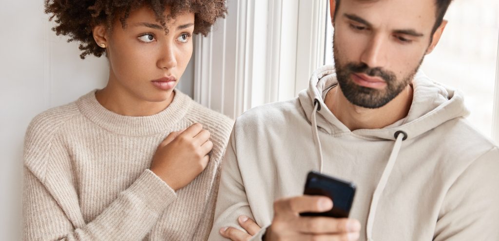 رجل يستخدم جوّاله وزوجته بجانبه تنظر إليه بحزن