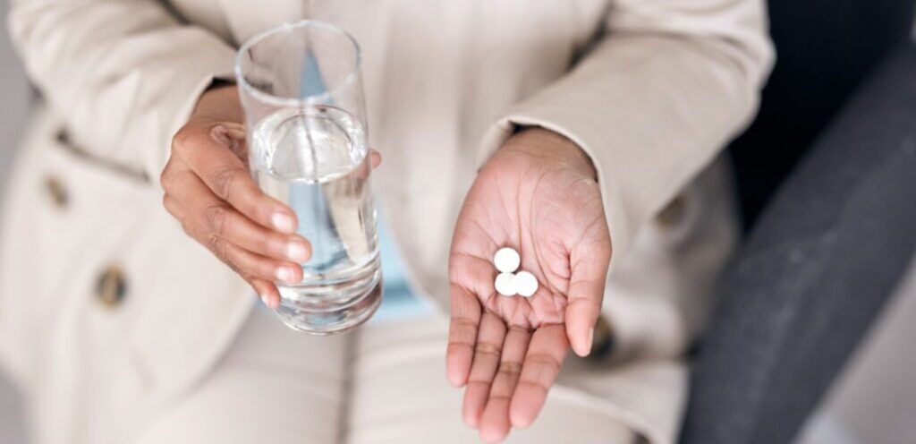 امرأة تمسك حبوب دواء وكوب من الماء