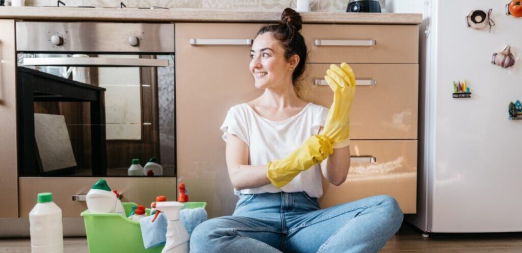 امرأة مبتسمة وبجانبها أدوات تنظيف منزلية