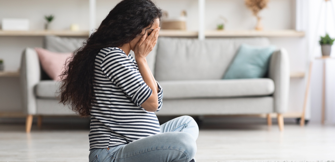 امرأة حامل حزينة تجلس على  الأرض وتضع يديها على وجهها