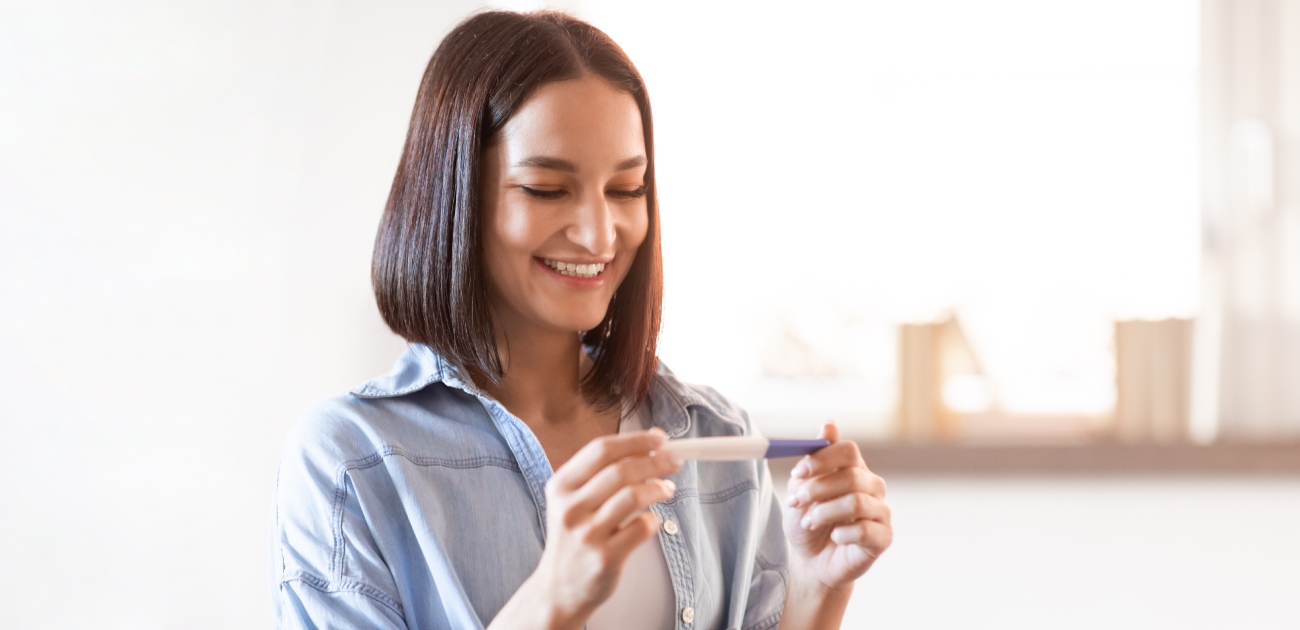 امرأة تمسك اختبار الحمل وتنظر إليه بسعادة